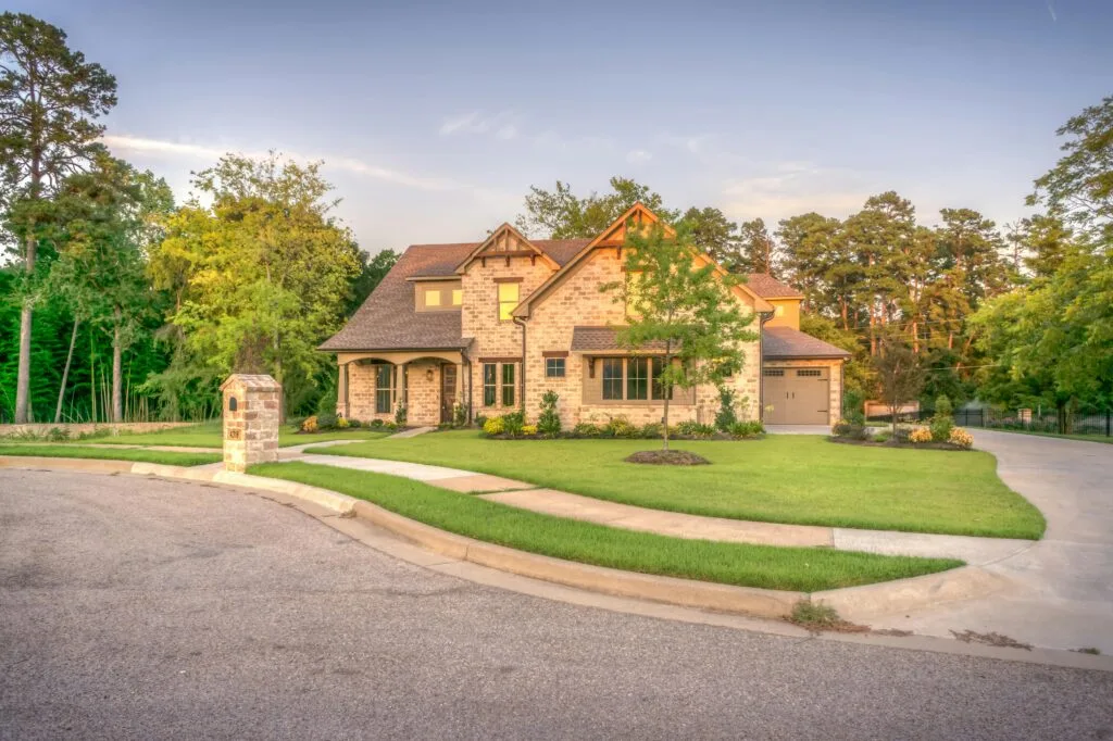 pexels-photo-259593-259593 Elegant stone family home with manicured lawn, trees, and driveway on a sunny day.