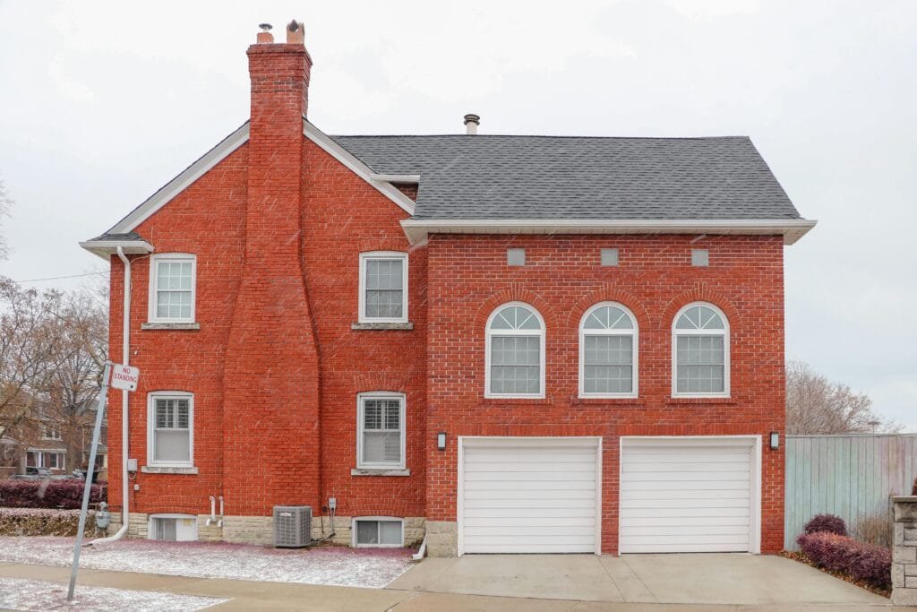 Red brick house exterior in Toronto with arched windows, chimney, and double garage.